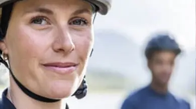 Frau mit Fahrradhelm schaut in Kamera, Mann mit Fahrradhelm im Hintergrund
