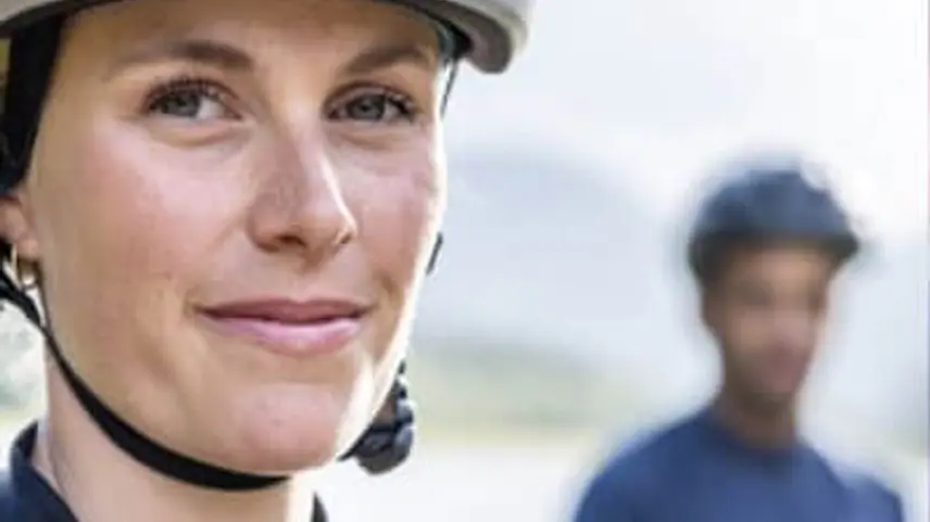 Frau mit Fahrradhelm schaut in Kamera, Mann mit Fahrradhelm im Hintergrund