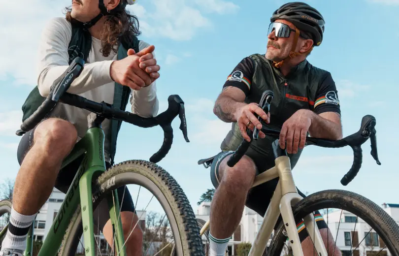 Zwei Männer auf Gravelbikes, sie stehen und lehnen sich auf ihre Lenker
